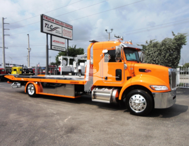 Peterbilt 337 tow truck/rollback orange cab and flatbed from side view with TLC sign in background