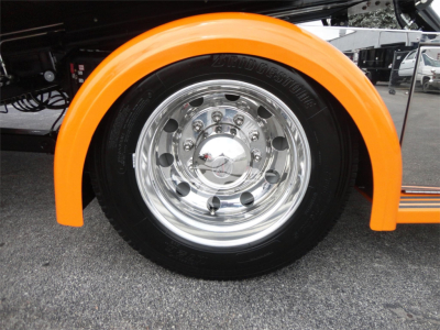 Peterbilt 337 wheel with bright orange fender, chrome hubcap and tire under the truck.