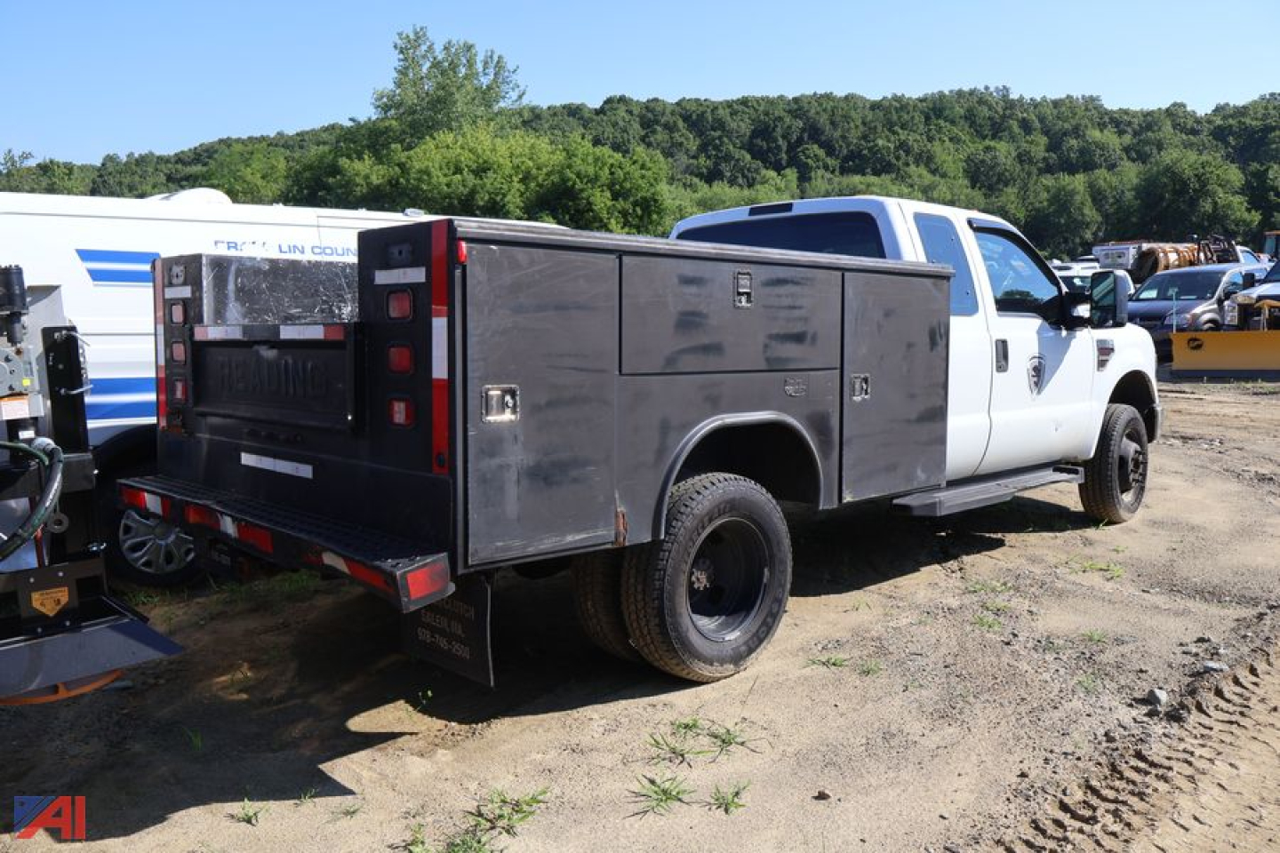 2008 Ford F-350 Super Duty utility truck in a salvage yard, long white cab with heavy black utility bed, service body with compartments, rear wheels dual, dirt ground.