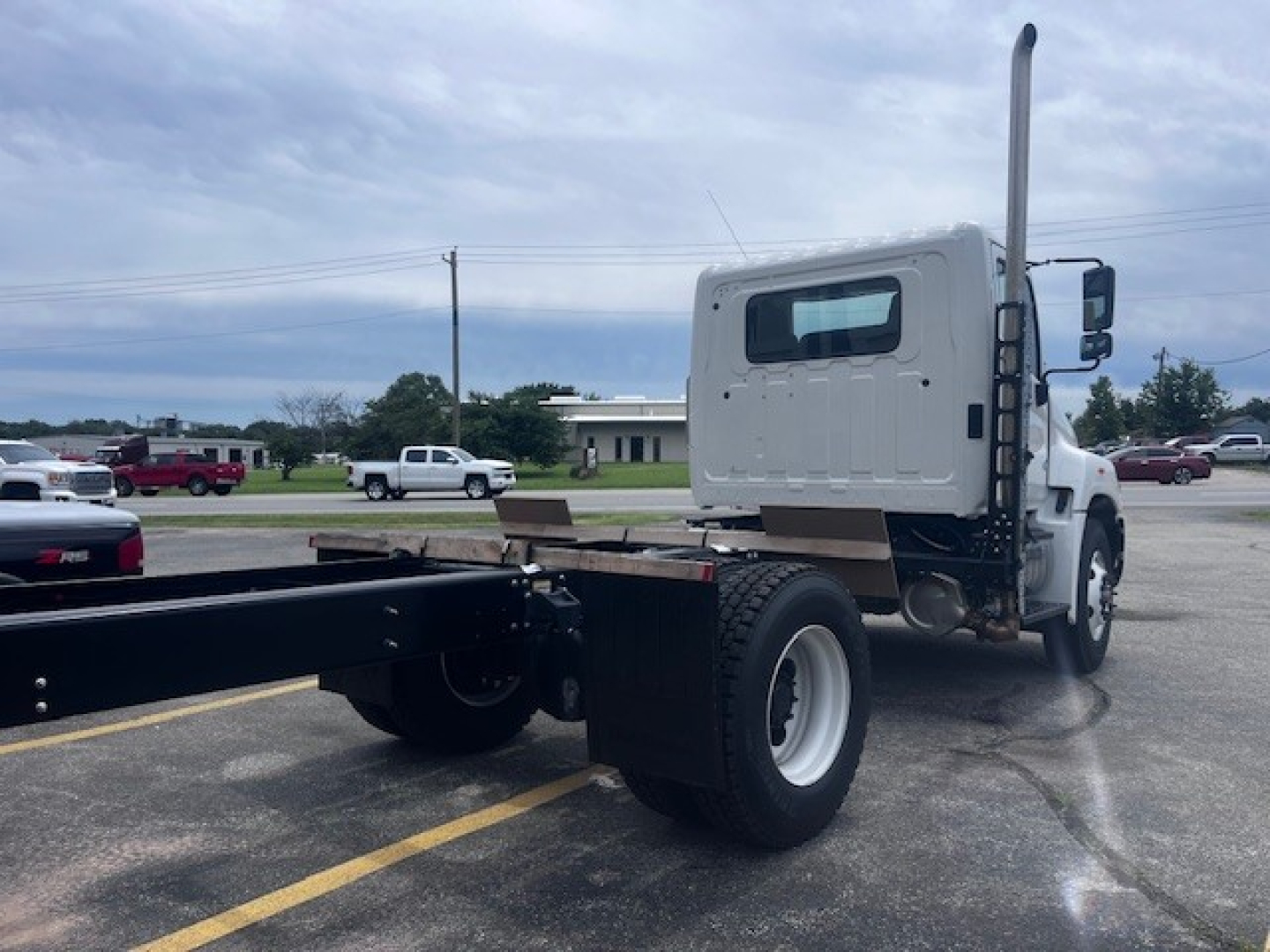 Truck cab and chassis rear-right side showing white sleeper cab, long chassis, single rear axle, and fuel tanks. Text not visible in image
