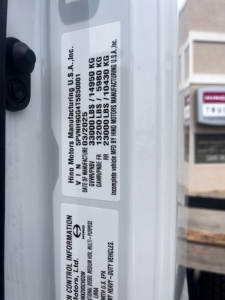 Label on Hino XL7 cab and chassis showing VIN, stock number, and manufacturer information with weight specs.