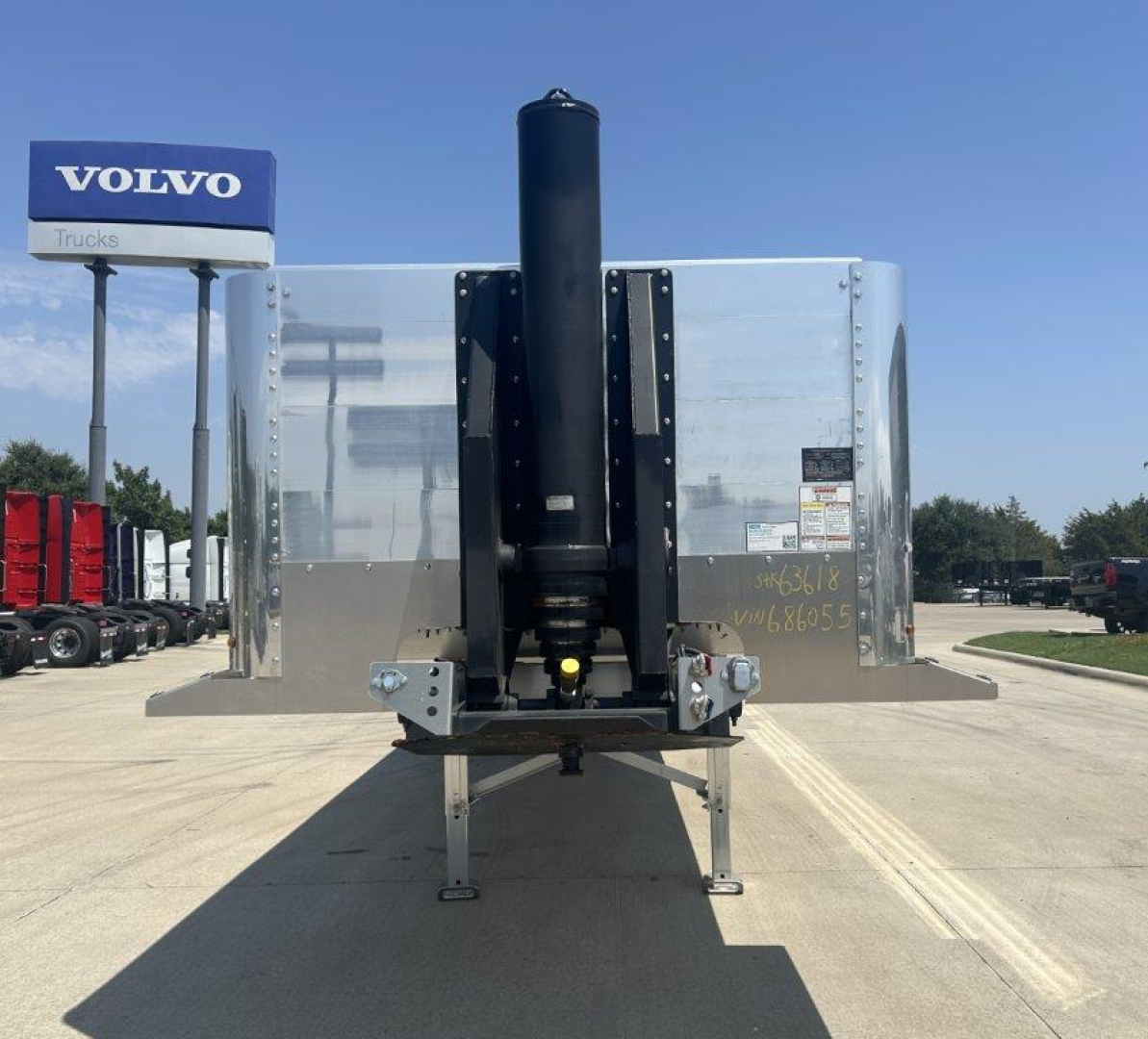 Trailer front view showing hydraulic tailgate hoist and silver dump body with black central support, Volvo truck sign in background.