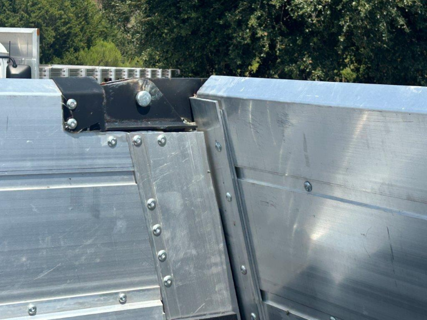 Dump trailer interior corner with metal panels and riveted joints, showing aluminum sidewall and hinge brackets.