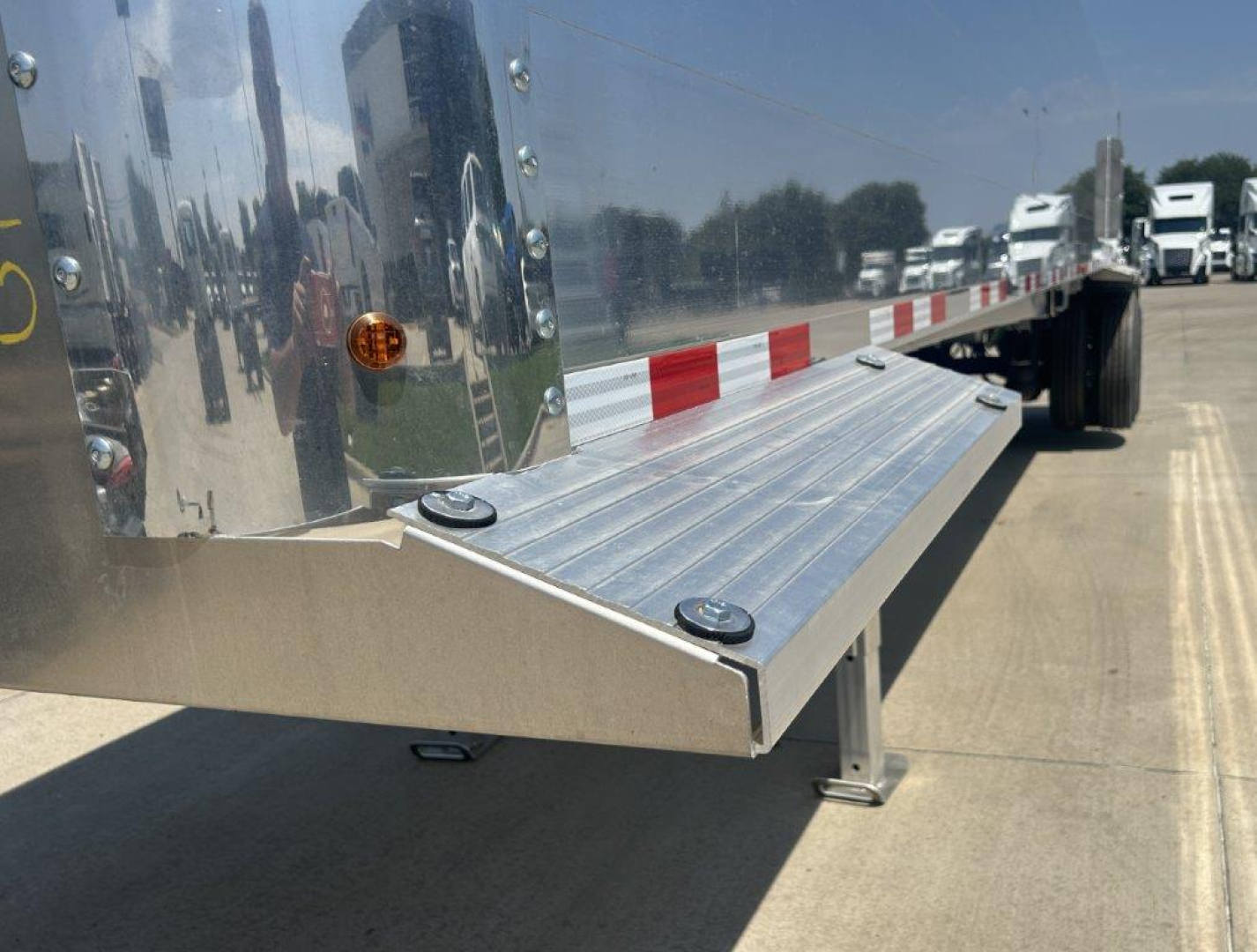 Dump trailer side with aluminum step/board extended, reflective chrome surface, landing pad and support leg.