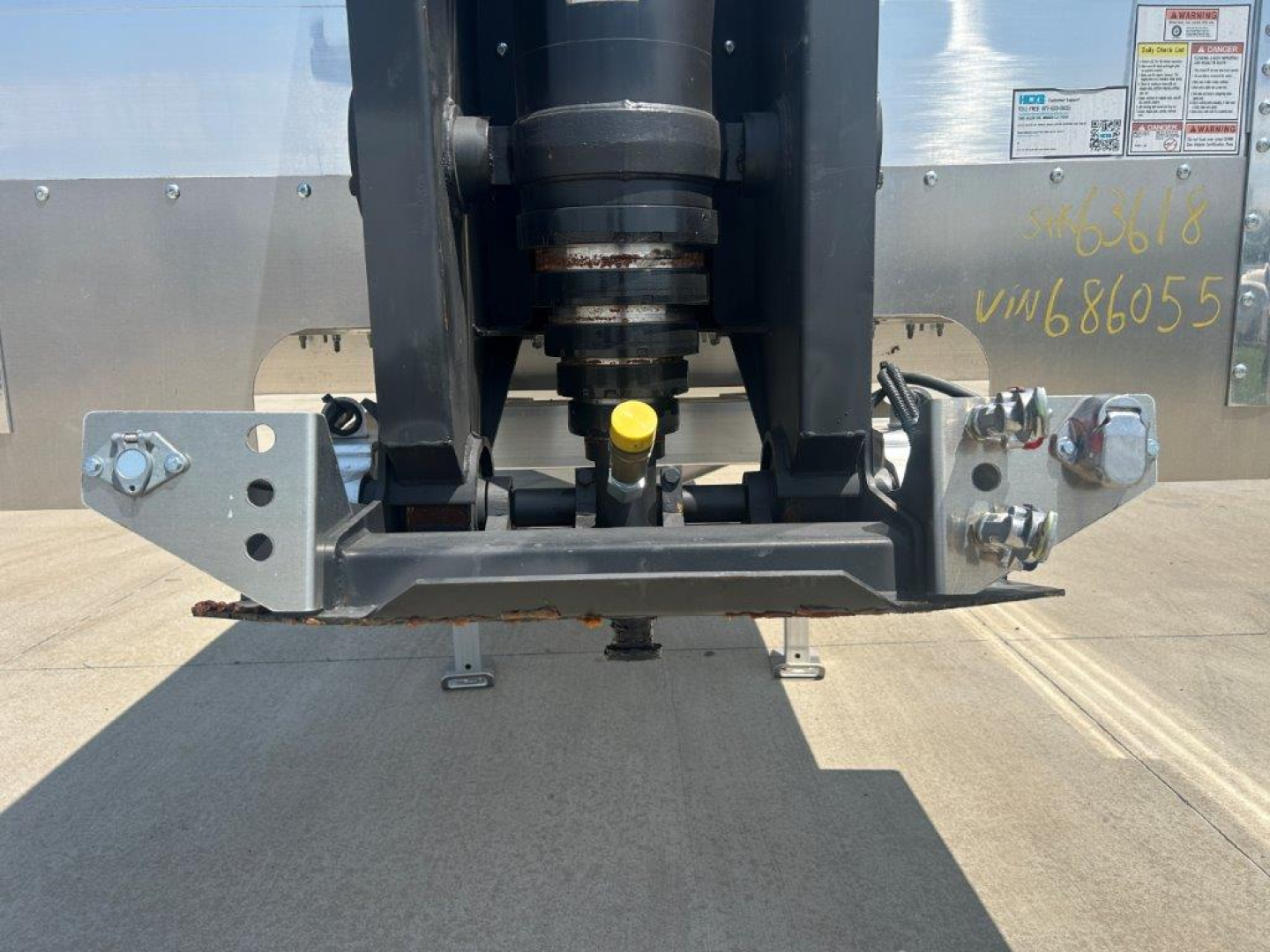 Trailer coupling and front hitch assembly showing mounting brackets, hydraulic kingpin, and yellow plastic cap in center; reflective metal trailer body with decals and screws.