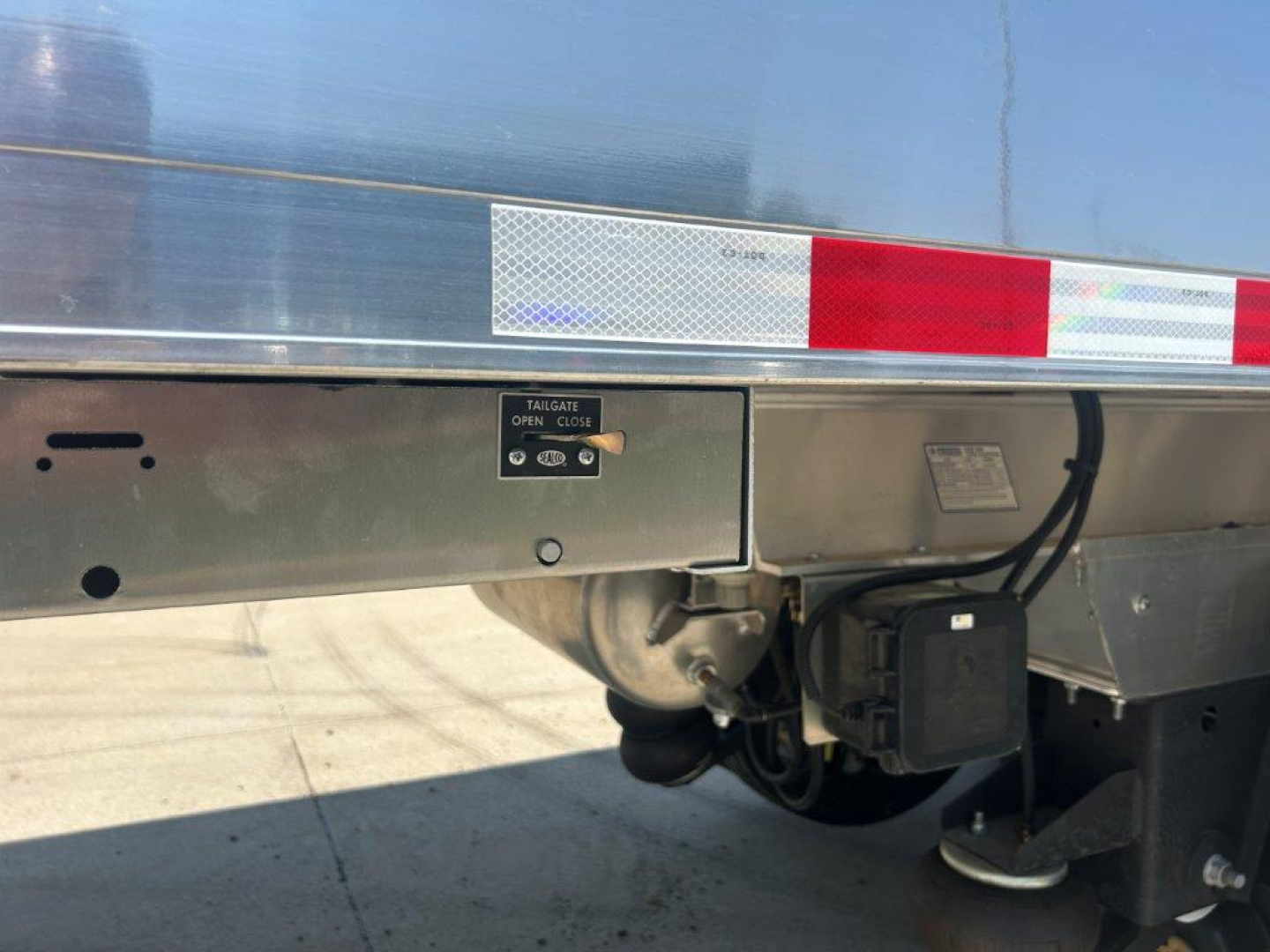 Trailer rear side showing taillight/marker assembly, reflective stripes, and a tailgate latch on a Hicks SL3729 dump trailer.