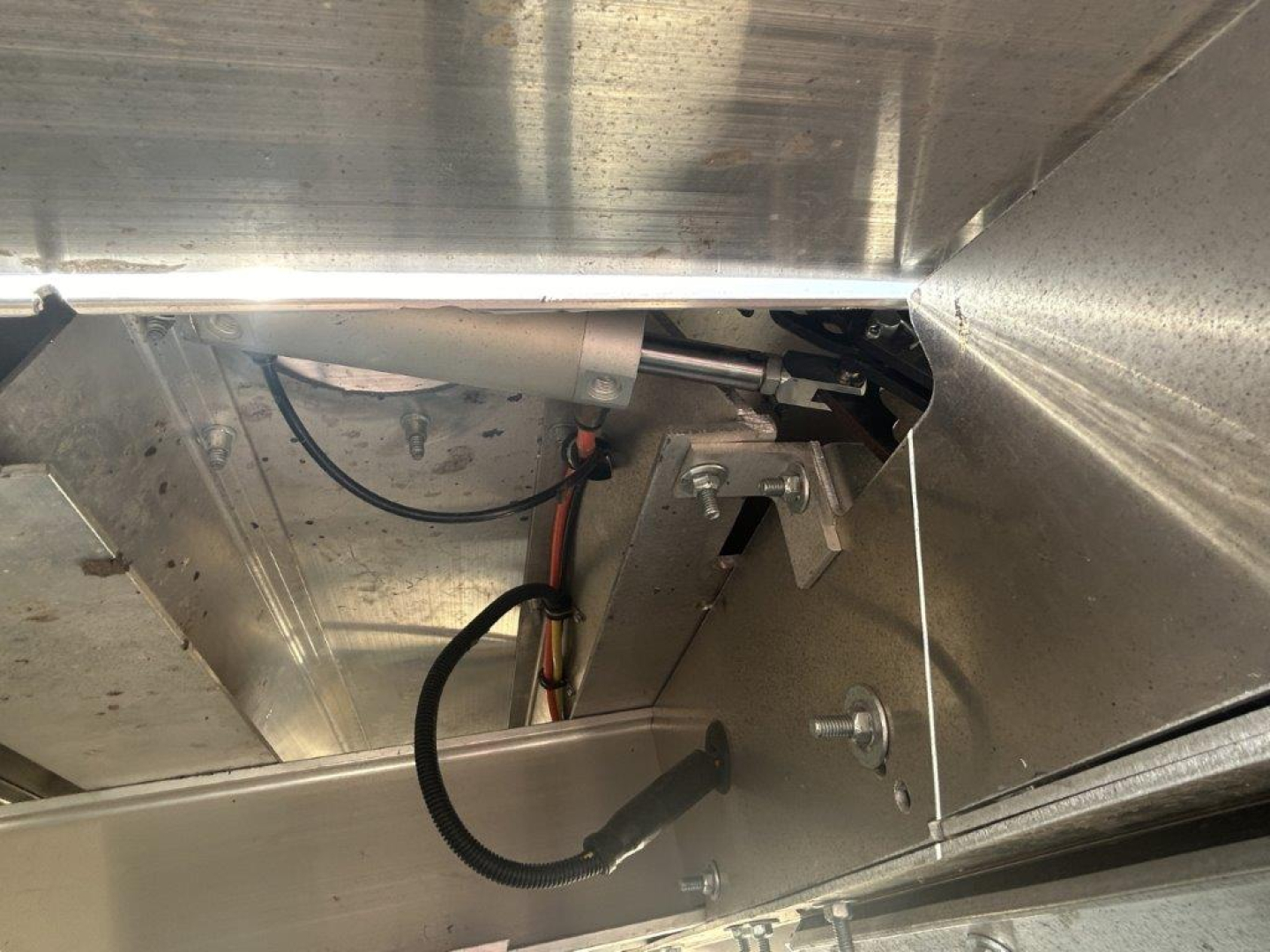 Dump trailer undercarriage close-up showing wiring harness and metal framing with bolts and a black wiring sleeve.