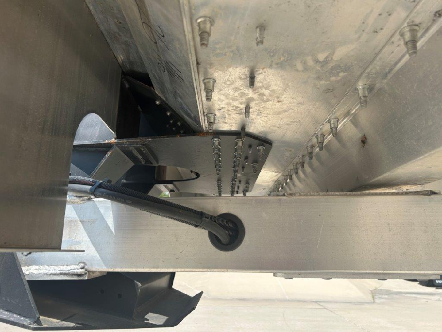 Trailer undercarriage with hydraulic landing gear, silver steel frame, and underside components visible in a dump trailer.