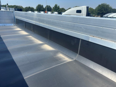 Dump trailer bed with aluminum sidewalls and smooth metal surface, viewed from inside the trailer showing the railing and interior wall.