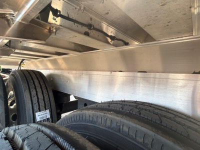 Dump trailer undercarriage showing tandem axles and aluminum frame with tires and suspension components.