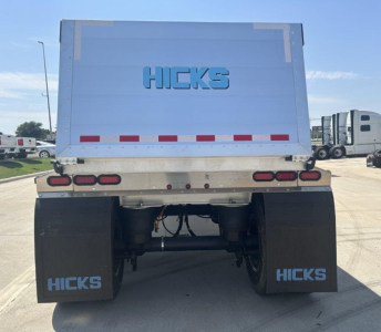 Rear view of a Hicks dump trailer showing the HICKS logo on the tailgate and mud flaps, with red and white reflective tape and the undercarriage visible.