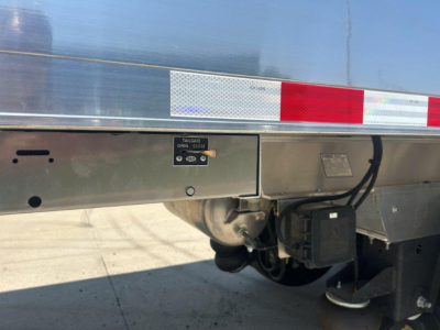 Trailer rear side showing taillight/marker assembly, reflective stripes, and a tailgate latch on a Hicks SL3729 dump trailer.