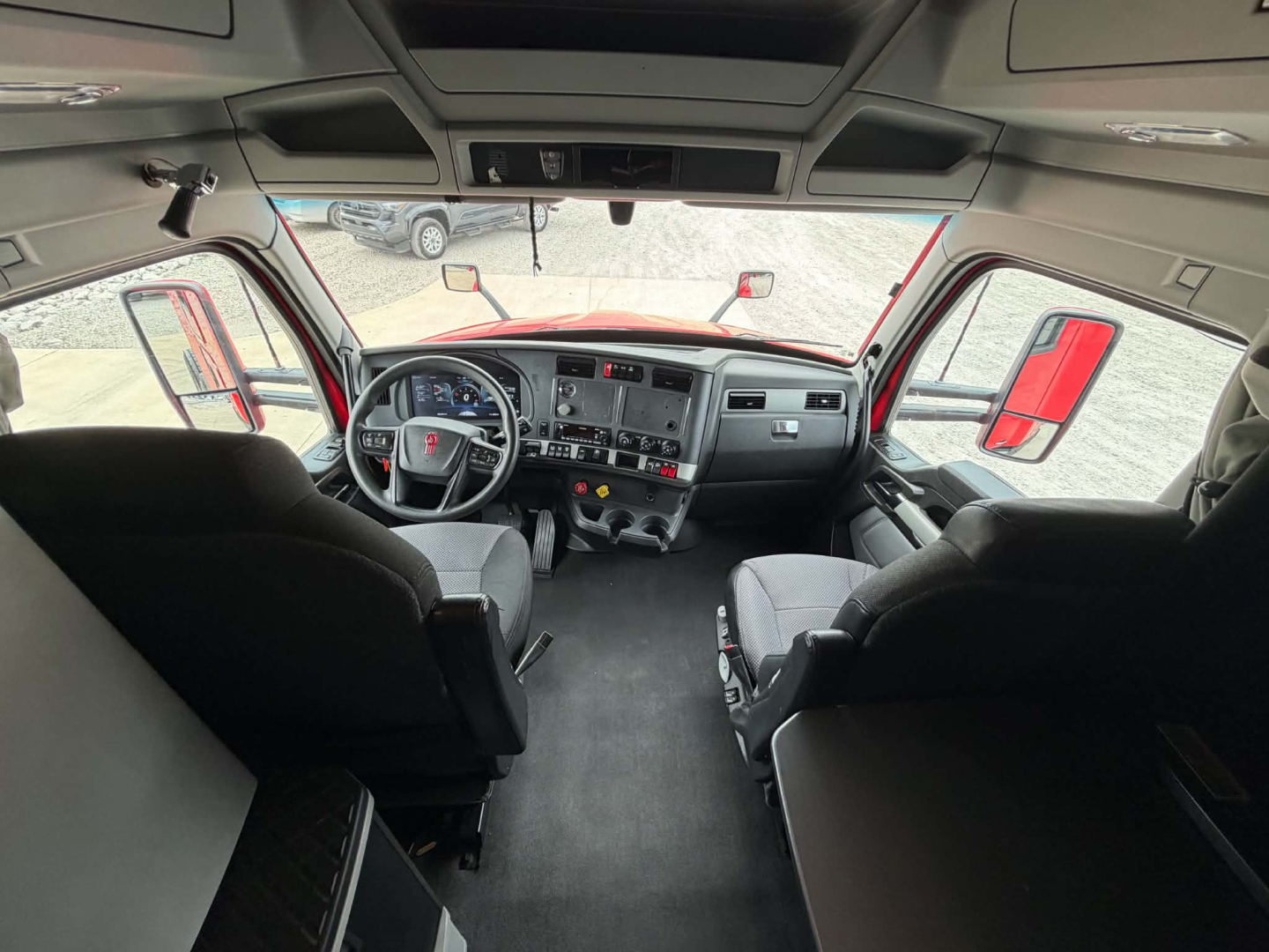Kenworth T680 cabin interior view from rear seating area showing dashboard, steering wheel, and overhead storage.