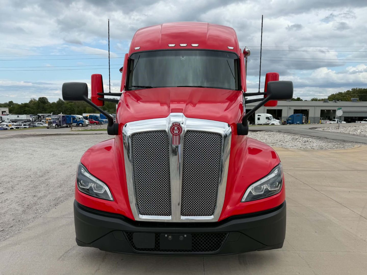 Front view of a red 2023 Kenworth T680 conventional sleeper truck showing chrome grille and emblem, black bumper, and side mirrors.