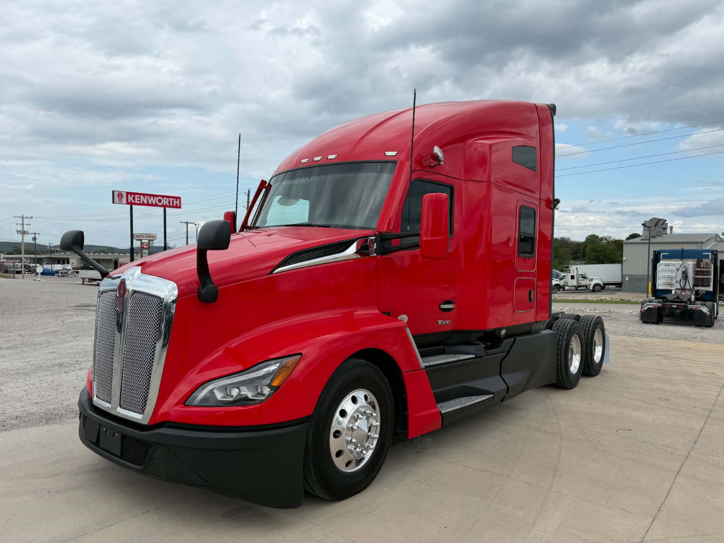 Kenworth T680 tractor red cab, side view showing sleeper, dual rear axles, large chrome grille, aerodynamic mirrors, daytime running lights.