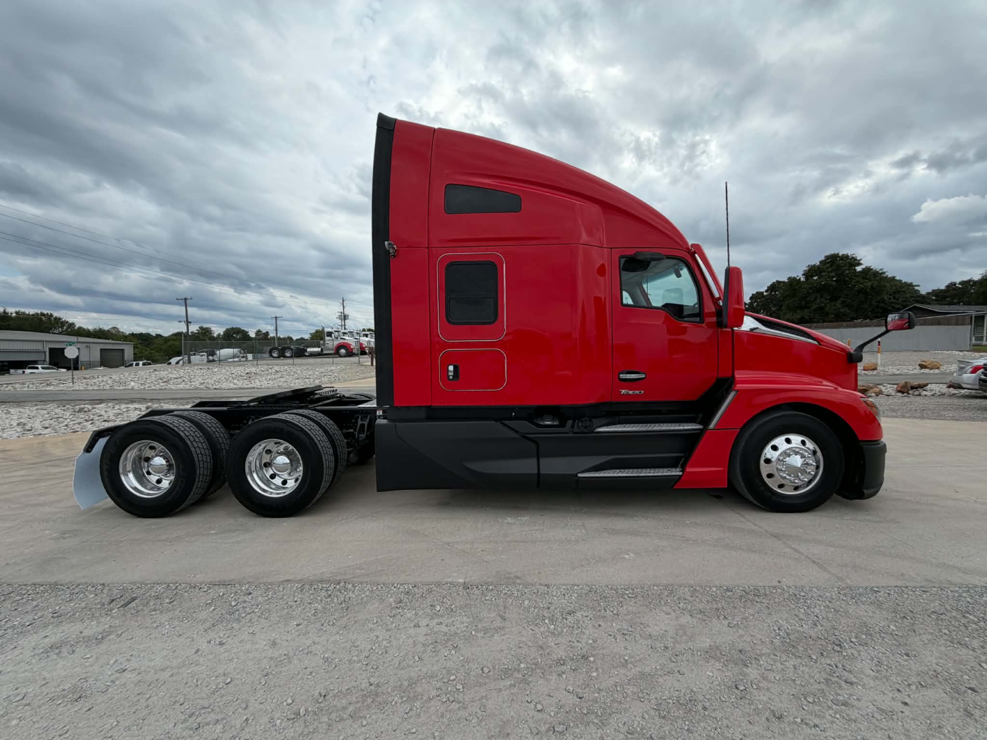 Kenworth T680 tractor-trailer side view showing red cab and sleeper, with triple rear axles, black lower body trim, and cloudy sky.
