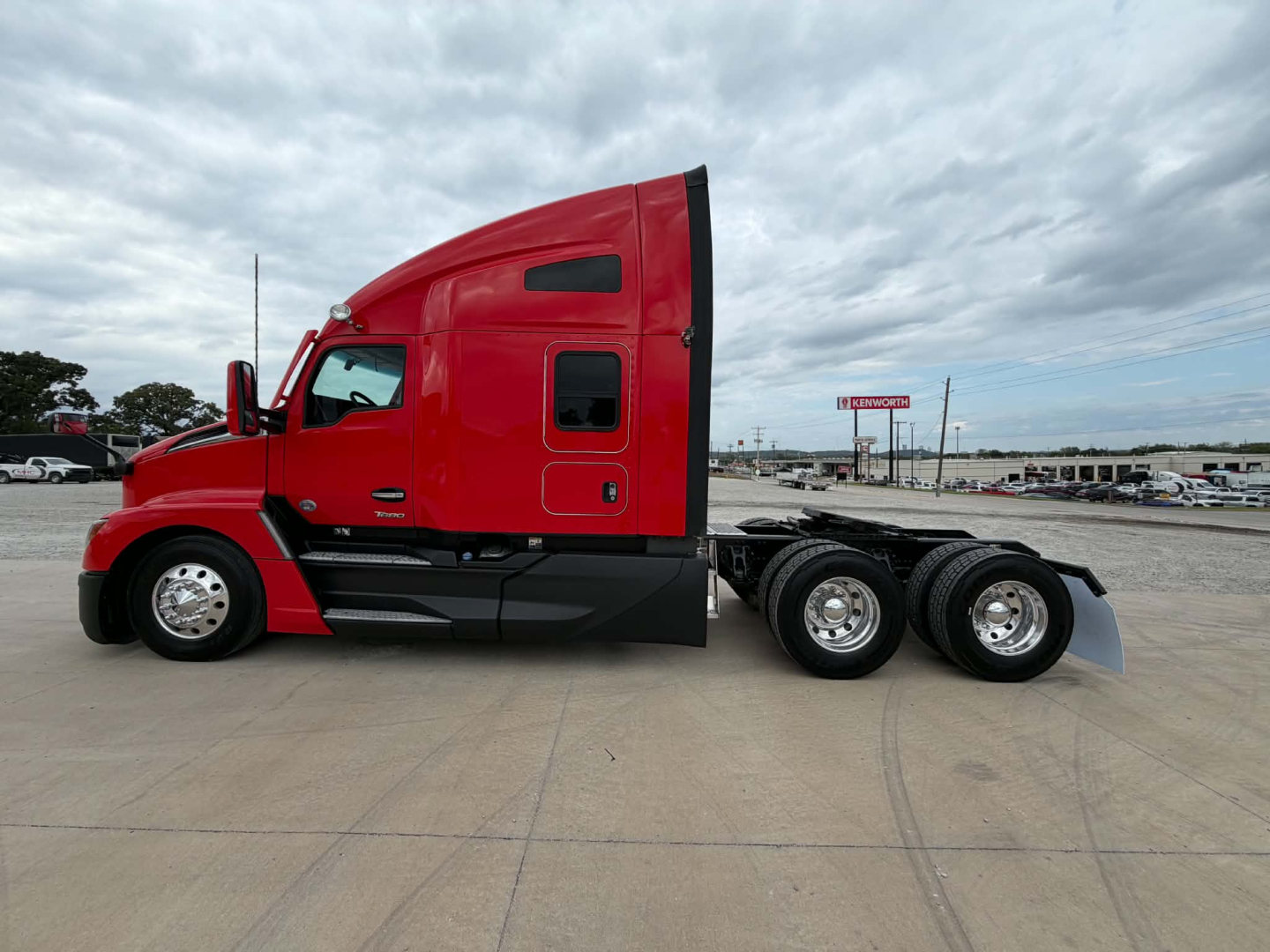 Kenworth T680 side view shows red cab and sleeper with triple rear axles, fuel tanks and steps visible.