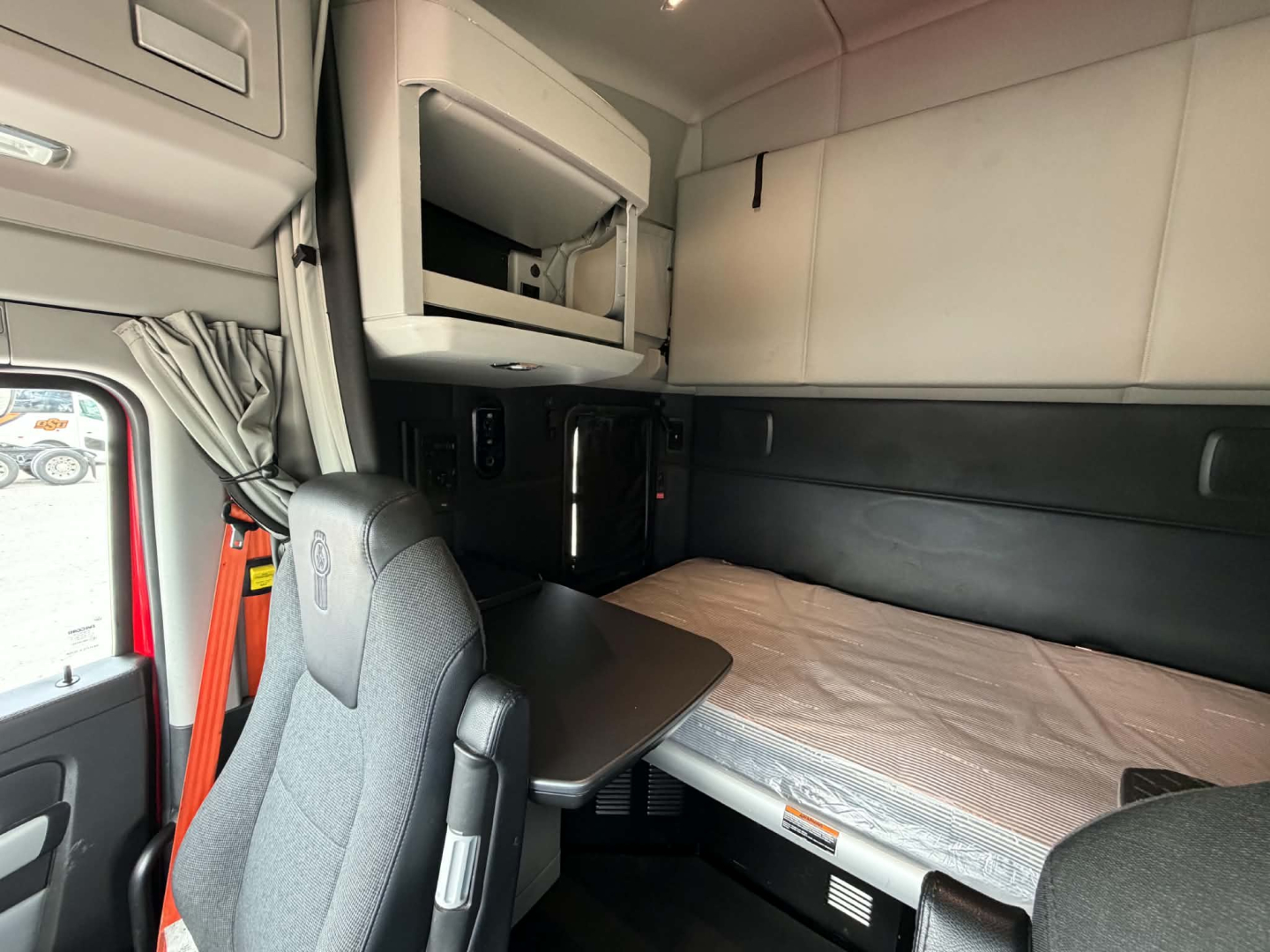 Kenworth T680 sleeper cab interior showing bunk bed and overhead storage.