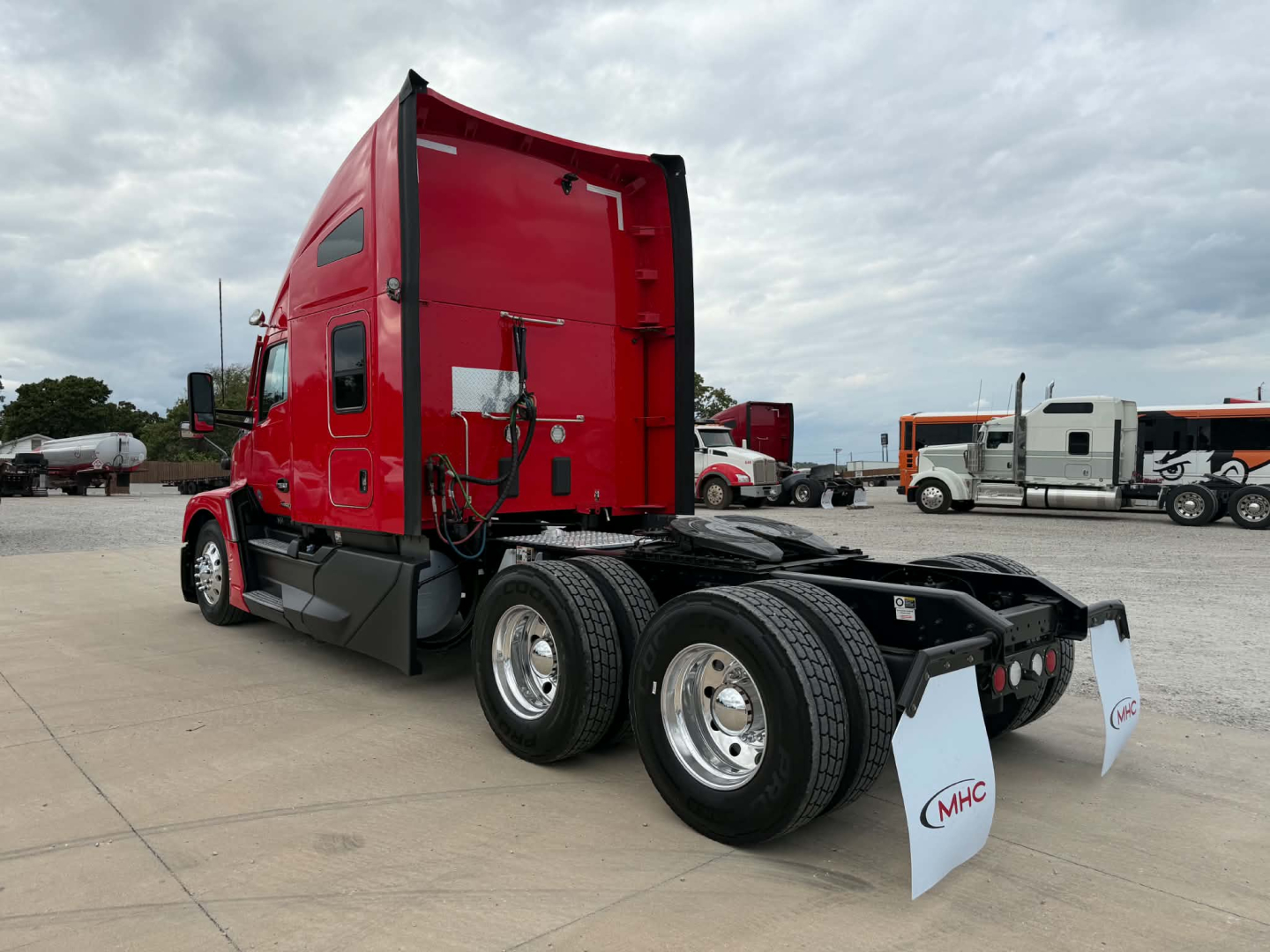 Kenworth T680 rear view showing dual rear axles on a highway tractor with red cab and white mud flaps, in a truck lot.