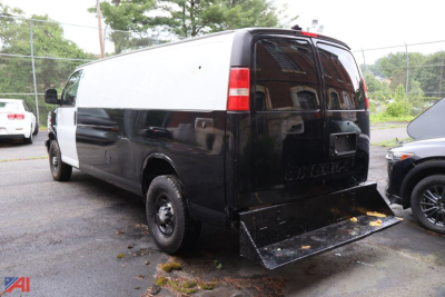 Rear-view of a black and white 2015 Chevrolet Express cargo van with a metal ramp at the back, police vehicle style with windowed rear doors and high roof.