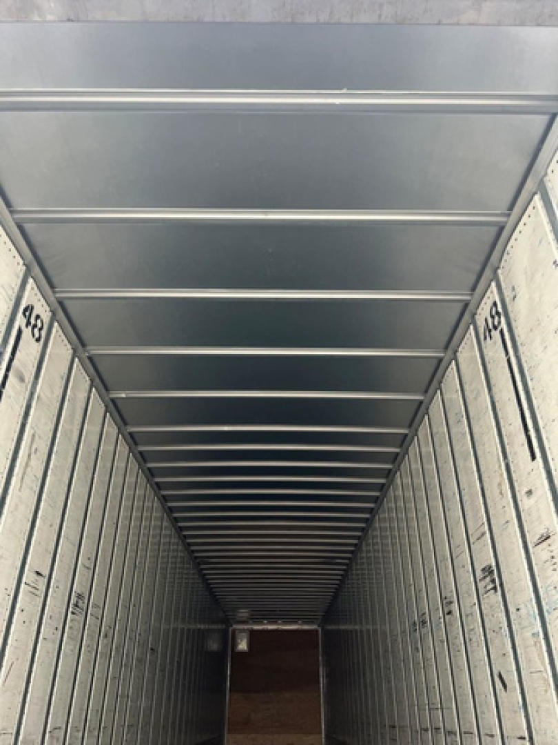 Trailer interior with corrugated metal walls and overhead ceiling beams in a long empty loading space.