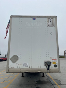 Rear view of a white utility van trailer showing DOT rear doors, latching mechanism, and small ventilation/inspection decals.