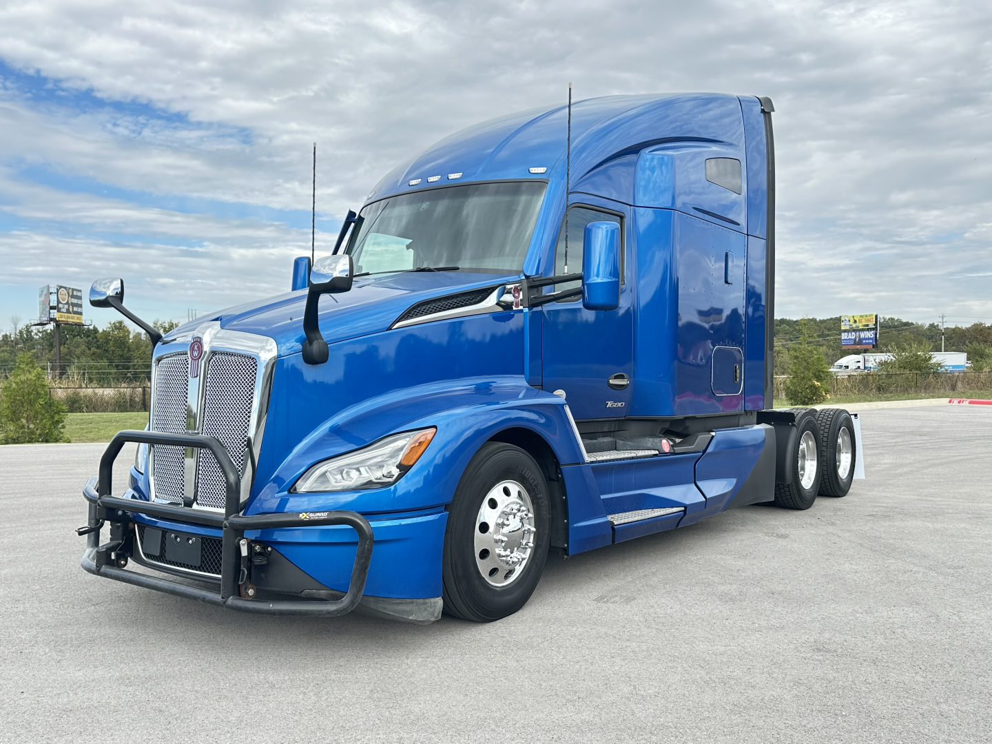 Kenworth T680 tractor unit in blue with front bull bar and sleeper cab, side view showing tandem rear axles