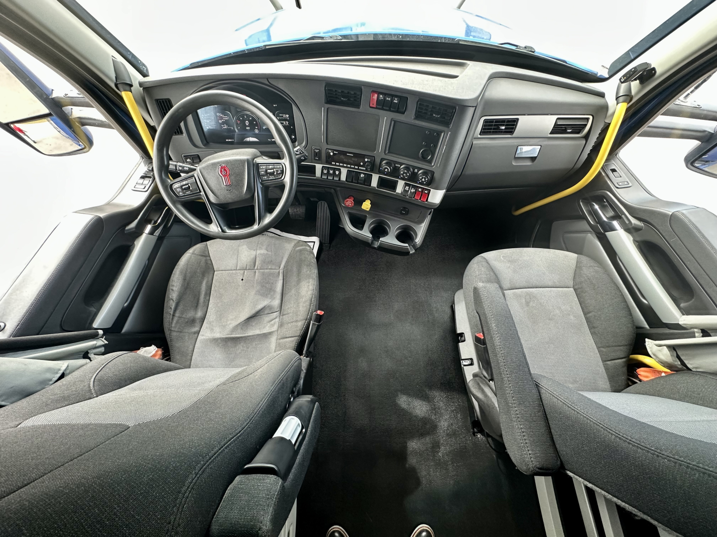 Kenworth T680 cab interior with steering wheel, dashboard, and two front seats visible from a wide-angle view.