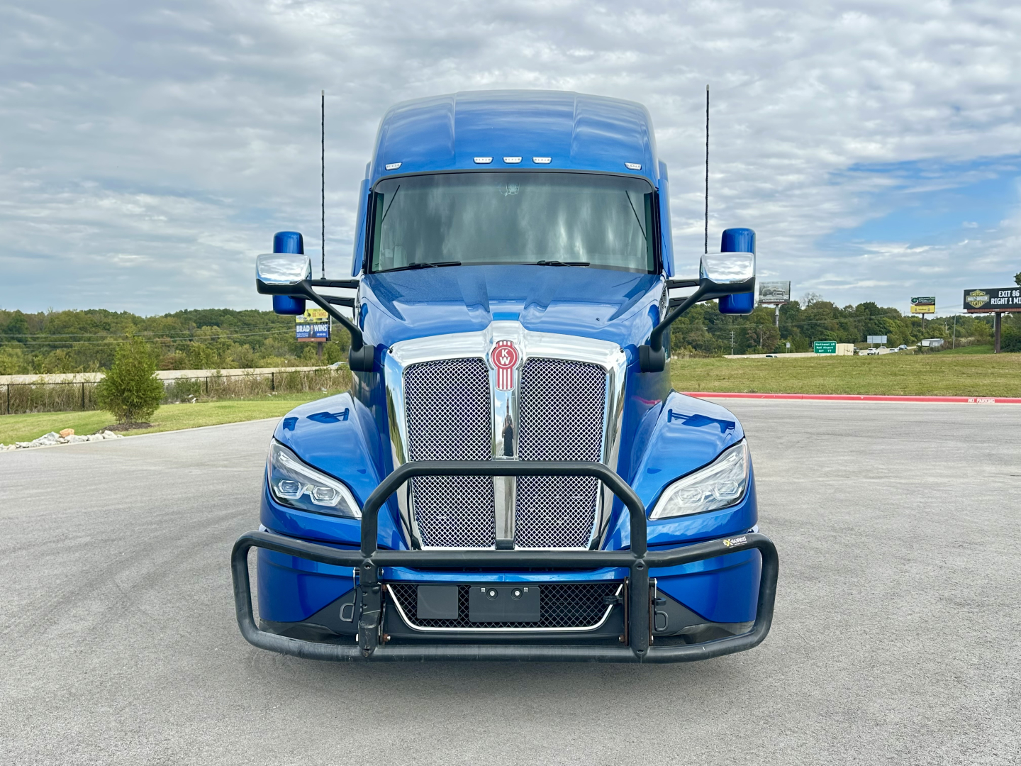Front view of a blue 2023 Kenworth T680 conventional sleeper truck with a bull bar guarding the chrome grille.
