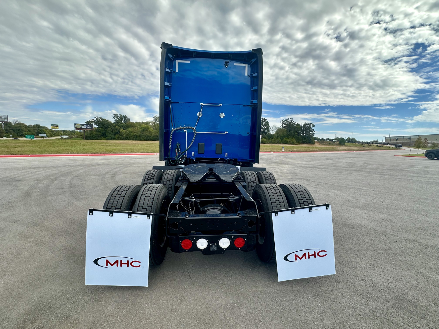 Kenworth T680 rear view showing blue cab interior and chassis with mud flaps labeled MHC, visible hitch and fuel lines.