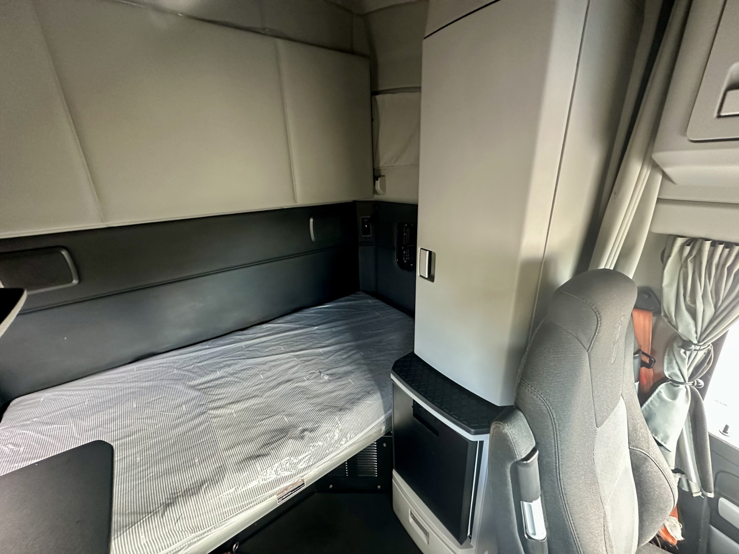 Interior sleeper area of a Kenworth T680 cab with bunk bed setup, visible mattress, and storage cabinet nearby.