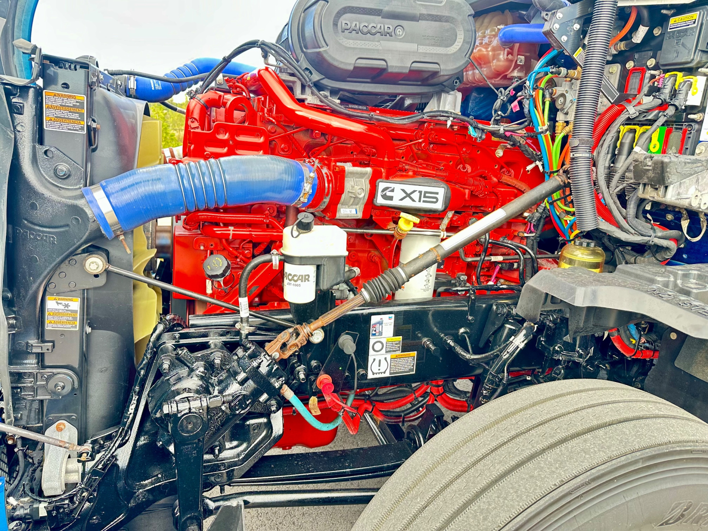 Harvester red Cummins X15 engine in engine bay of a Kenworth T680 truck showing engine components and blue intercooler hose.