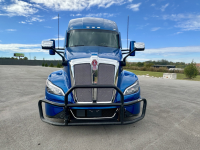 Kenworth T680 front view in blue with grille guard and chrome bumper, daytime outdoor lot.