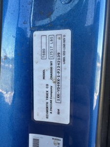 Kenworth T680 identification plate with model T680, chassis WV, weight labels, and VIN 1XKYD49X1PJ242139. Blue truck door area with sticker text.