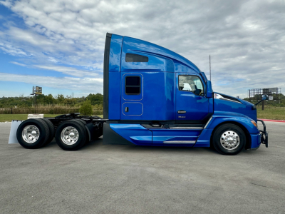 Kenworth T680 side view showing bright blue sleeper cab and tridem rear axle with six wheels.