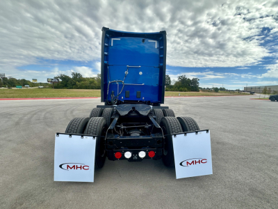 Kenworth T680 truck rear view showing blue cab interior and white mud flaps with MHC logo.