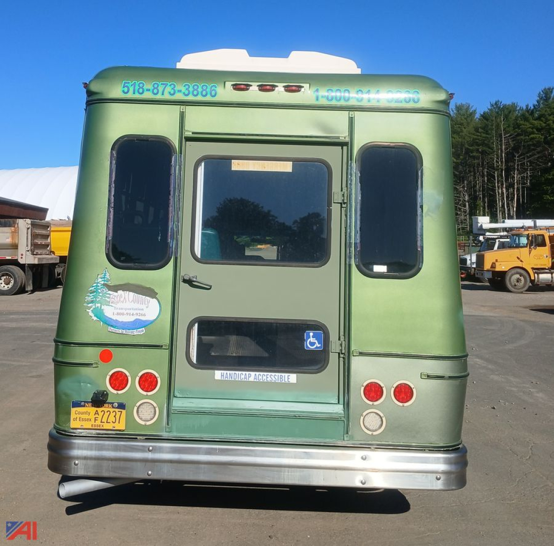 Ford E-450 wheelchair bus rear view showing handicap access sticker and license plate, with blue contact numbers on green body.