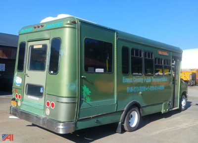 Ford E-450 shuttle bus in green with wheelchair ramp, rear view showing taillights and back doors, Riverside decals and bus windows.