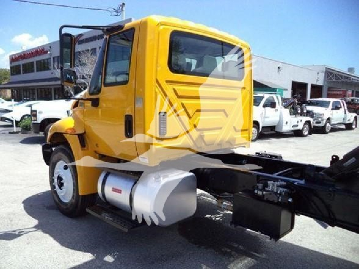 Yellow International 4300 truck cab with side fuel tank and chassis visible, dealership lot in background.