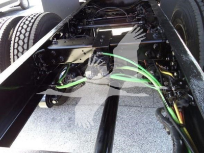 Truck chassis undercarriage showing green wiring harness and frame rails in a dump truck, with dual rear axles and suspension components visible.