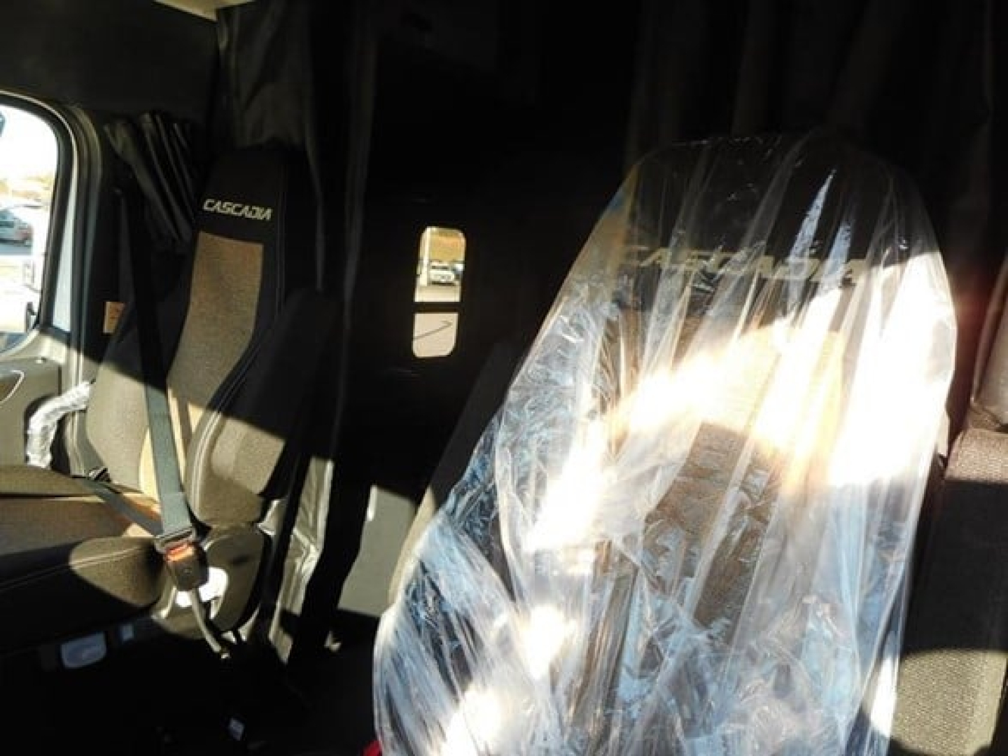Freightliner Cascadia 126 sleeper cab interior showing driver seat and passenger seat with protective plastic on the right seat.