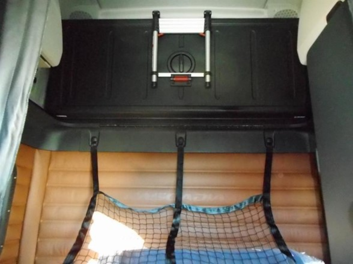 Freightliner Cascadia cab interior showing cargo storage area with tan ribbed mat and straps, view from sleeper area.