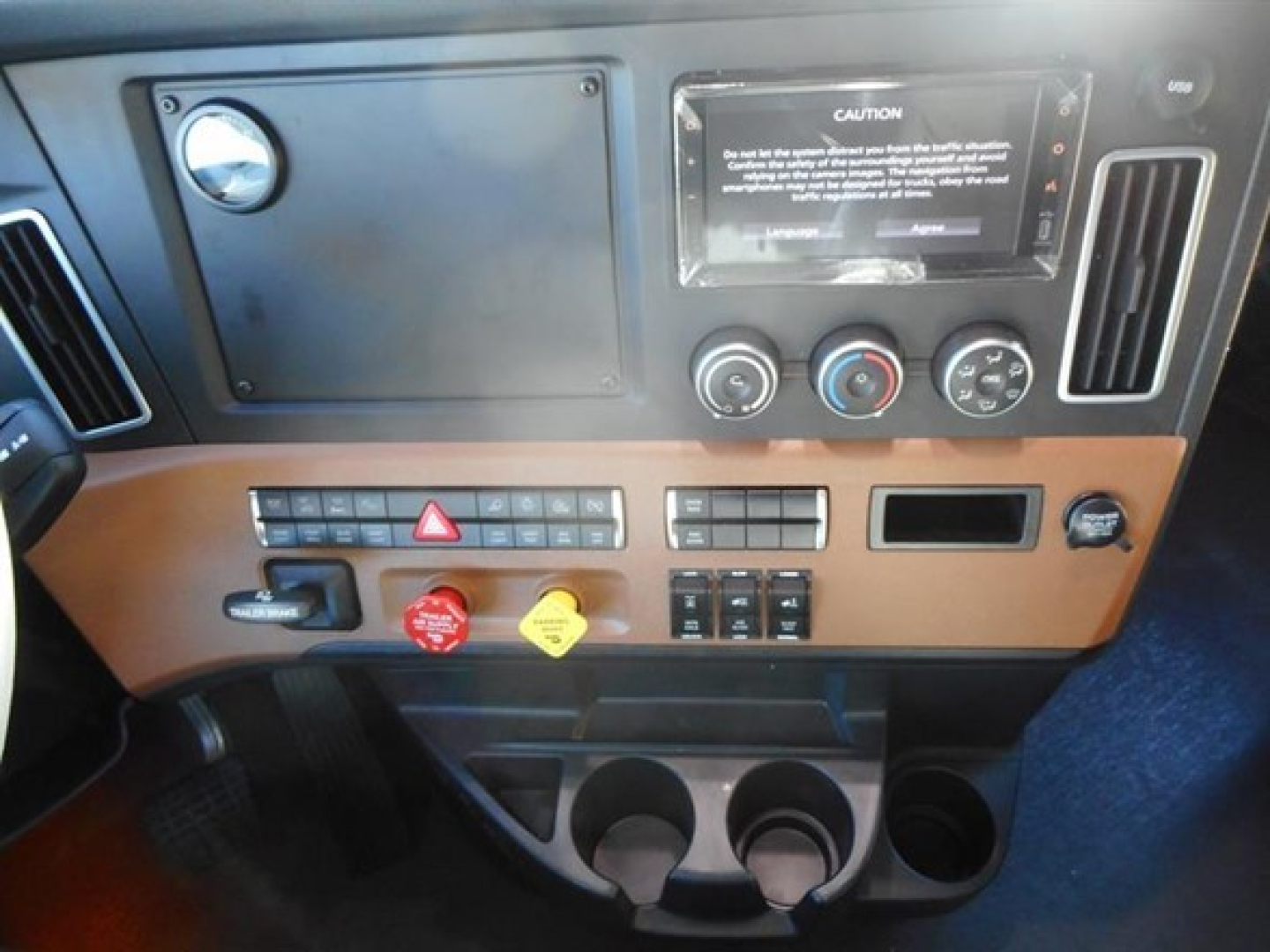 Dashboard of a 2026 Freightliner Cascadia 126 showing climate controls, hazard switch, cup holders, and a warning placard. Visible text includes caution label and various control labels.