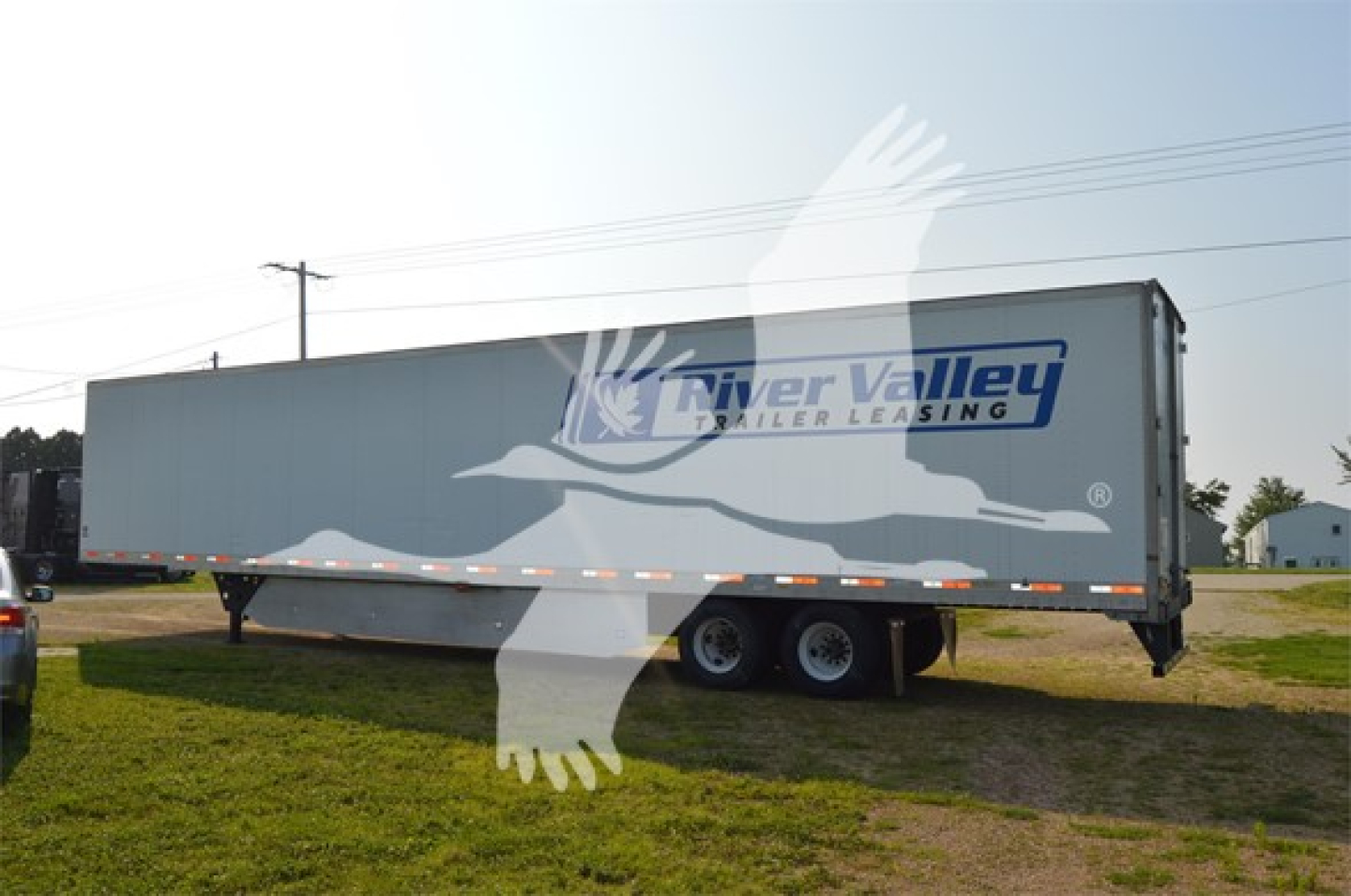 Trailer side view showing River Valley trailer leasing logo, long rectangular trailer with tandem axles in a field.