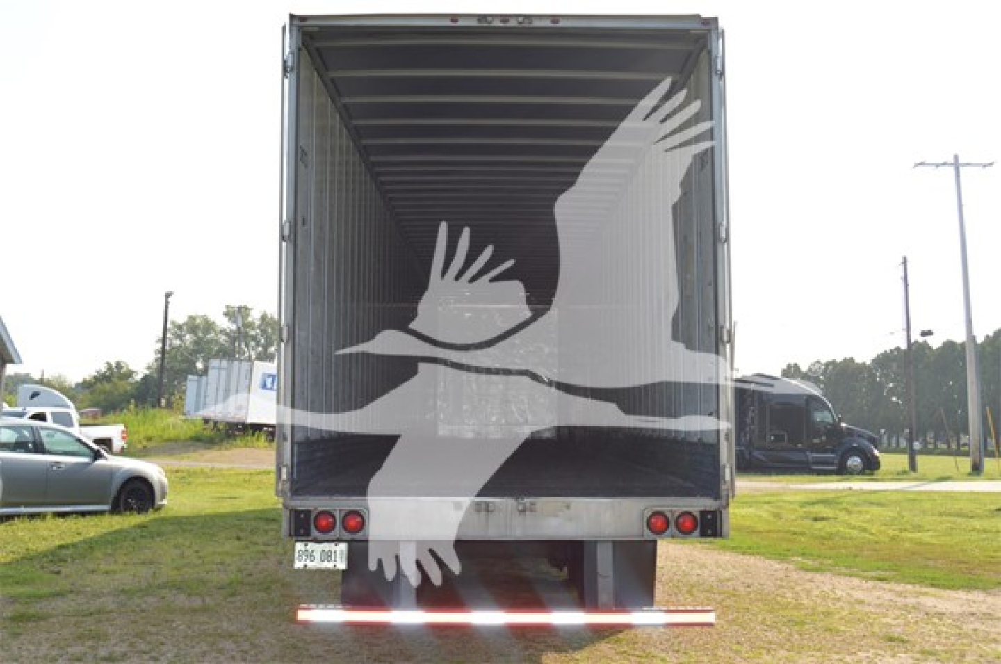 Truck trailer rear view showing back doors, tail lights, and a large white graphic of two birds in flight overlayed on doors.