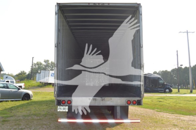 Truck trailer rear view showing back doors, tail lights, and a large white graphic of two birds in flight overlayed on doors.
