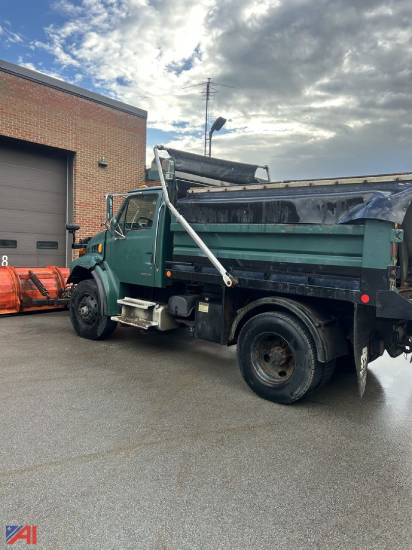 Dump truck from left-rear angle showing cargo bed, plow attachment, wing, and green cab with black dump body.