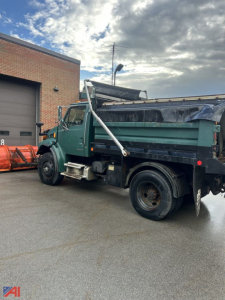 Dump truck from left-rear angle showing cargo bed, plow attachment, wing, and green cab with black dump body.