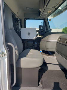 Cab interior of a Volvo VHD86B300 truck showing driver seat, steering column, dashboard, and a mounted white equipment box near the dash.