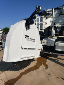Front view of a Tesmec Cleanfast trenching attachment on a Volvo VHD86B300 truck; white curved housing with Tesmec logo and mechanical arms visible.